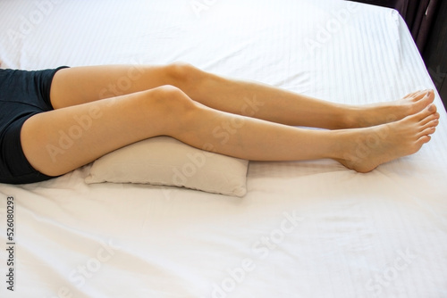 Billede på lærred Female with an anatomical pillow under her knees, lying on a bed with white sheets