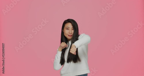 Cool asian modern young girl boxing at camera, punching with clenched fists. Battle, fight concept. Medium shot