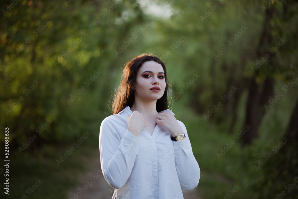 Sexy sensual brunette walks in a summer forest at sunset in a white blouse and jeans Sexy sensual brunette walks in a summer forest at sunset in a white blouse and jeans