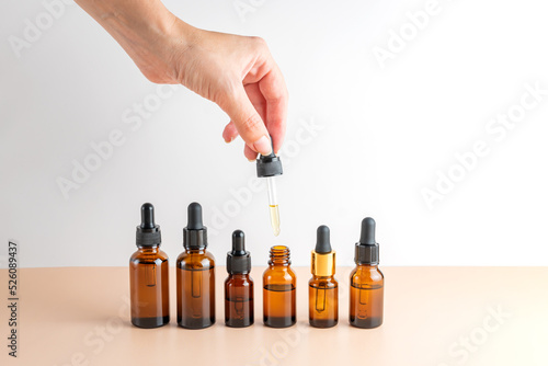 female hand with Dropper of essential oil, aromatherapy essence, assortment of beuty serums or medicinal liquid on beige background. Unbranded bottles for your design.