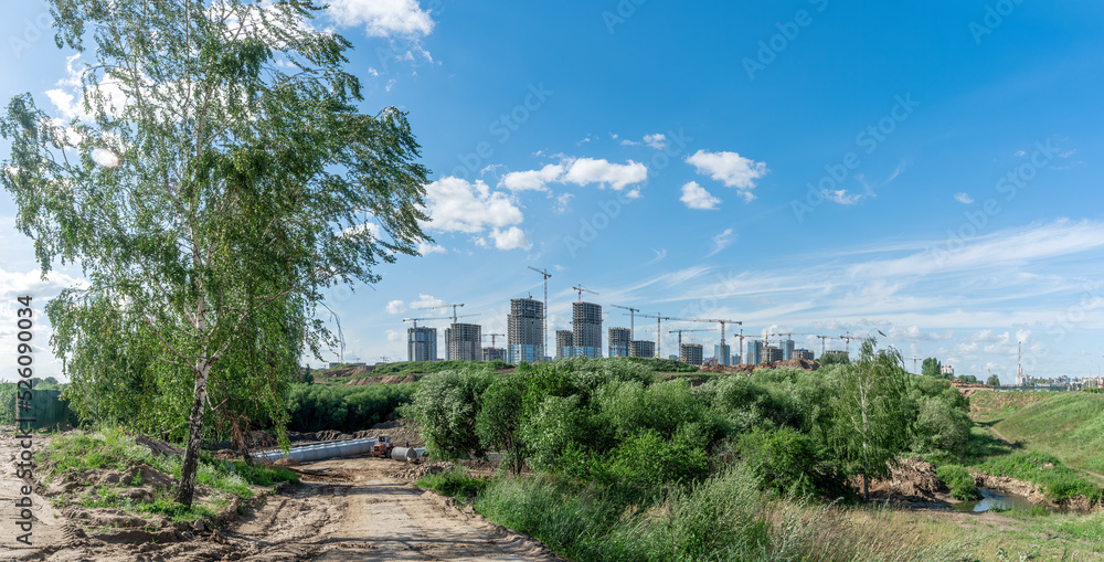 Construction of a multi-story residential buildings. Defocused foreground with young tree. Cranes work. Construction site.