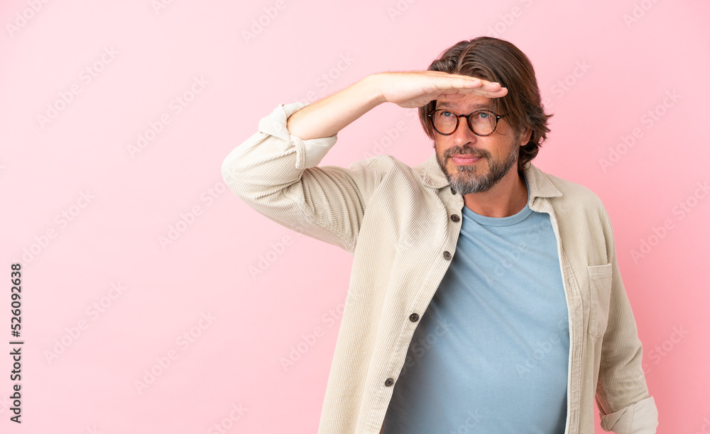 Senior dutch man isolated on pink background looking far away with hand to look something Senior dutch man isolated on pink background looking far away with hand to look something