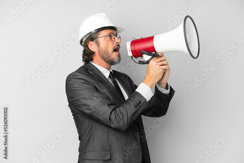 Young architect man with helmet over isolated background shouting through a megaphone
