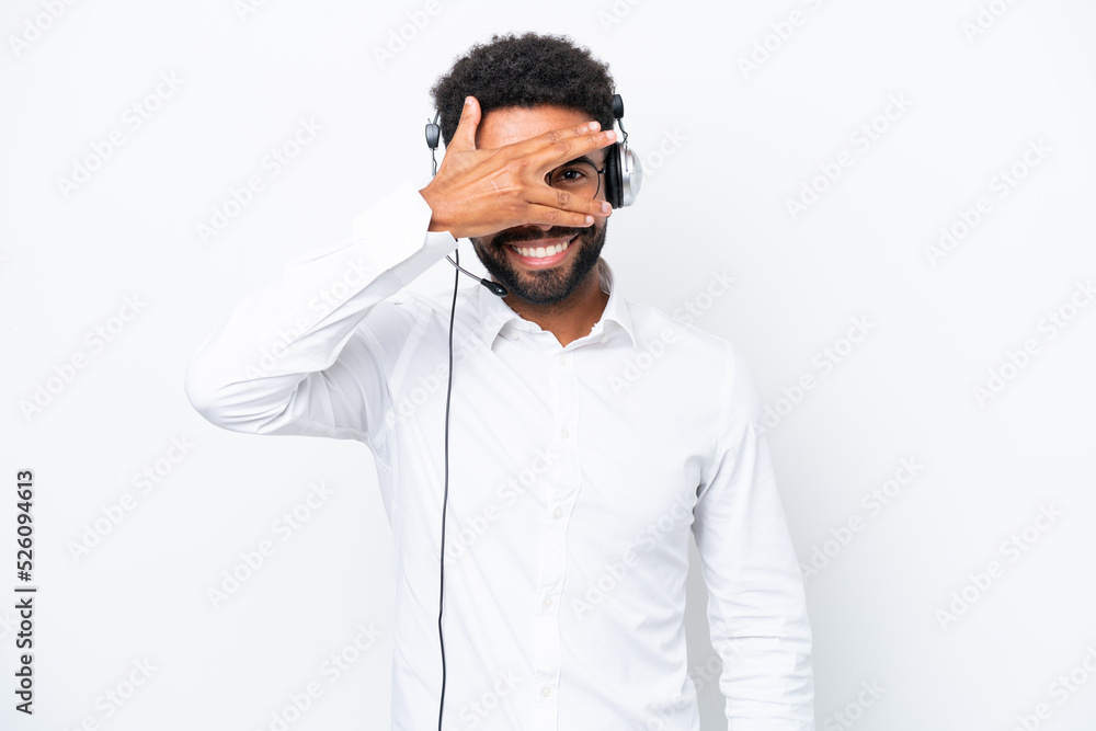 Telemarketer Brazilian man working with a headset isolated on white background covering eyes by hands and smiling Telemarketer Brazilian man working with a headset isolated on white background covering eyes by hands and smiling