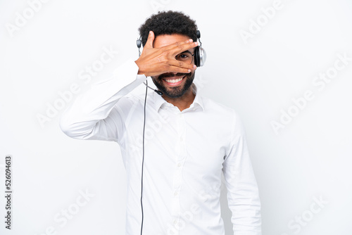 Telemarketer Brazilian man working with a headset isolated on white background covering eyes by hands and smiling © luismolinero