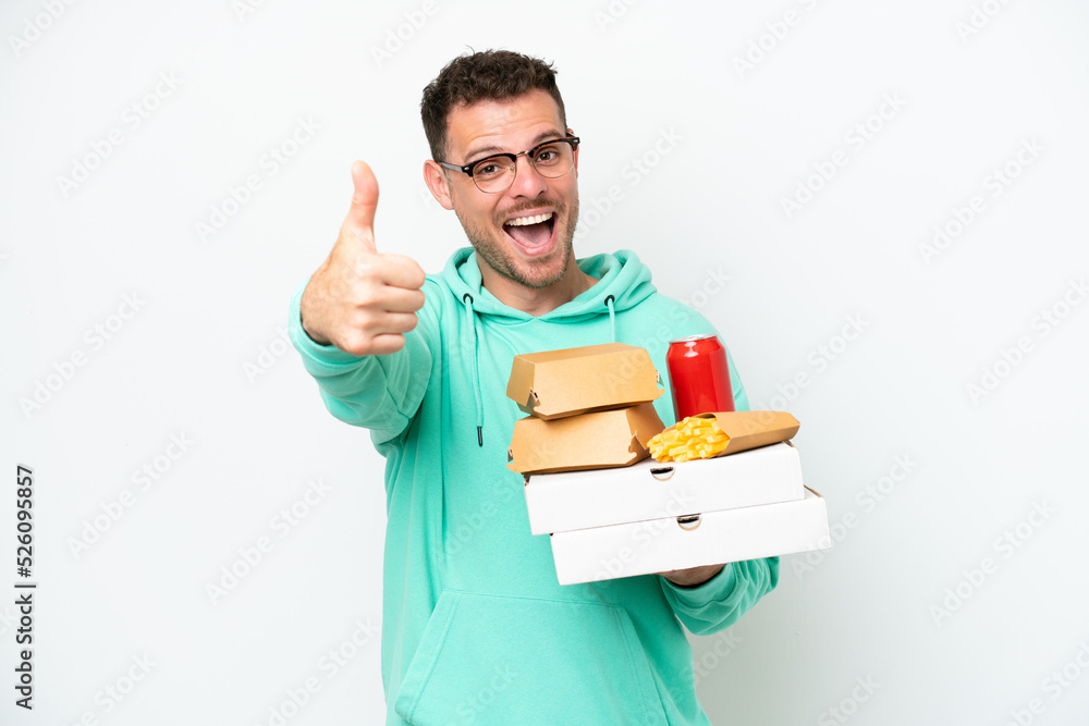 Young caucasian man holding fast food isolated on white background with thumbs up because something good has happened Young caucasian man holding fast food isolated on white background with thumbs up because something good has happened