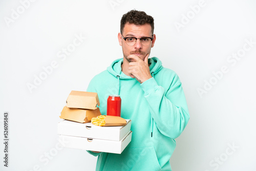 Young caucasian man holding fast food isolated on white background thinking