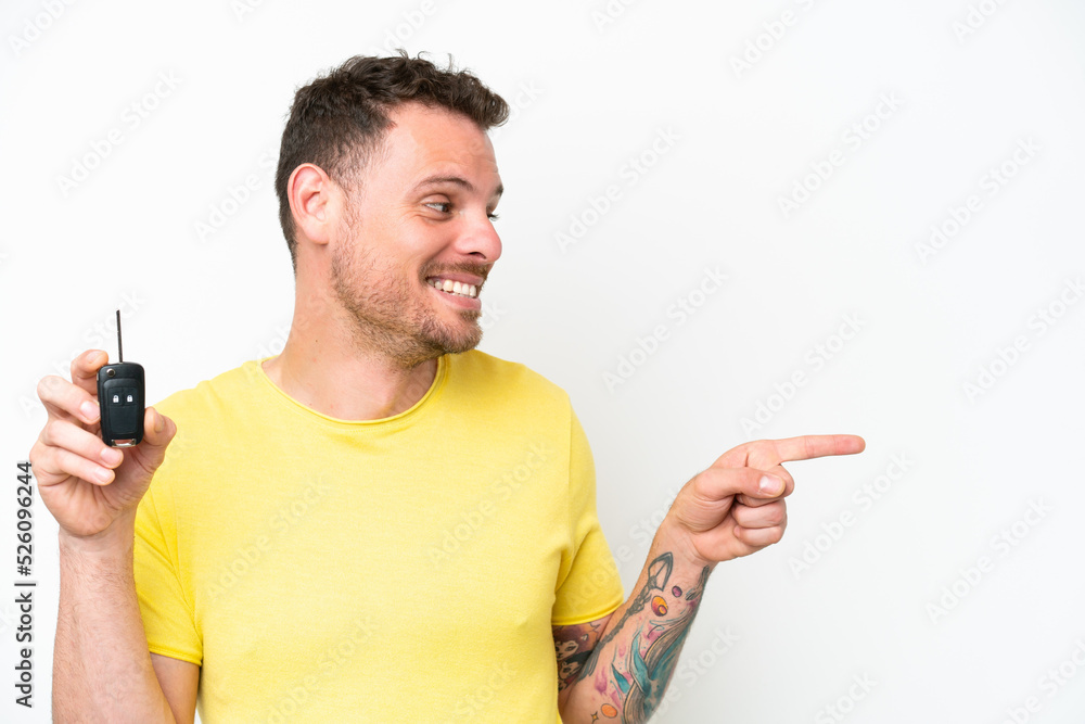 Young man holding car keys isolated on white background pointing to the side to present a product Young man holding car keys isolated on white background pointing to the side to present a product