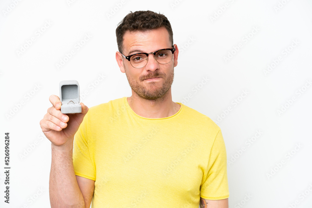 Young caucasian man holding a engagement ring isolated on white background with sad expression Young caucasian man holding a engagement ring isolated on white background with sad expression