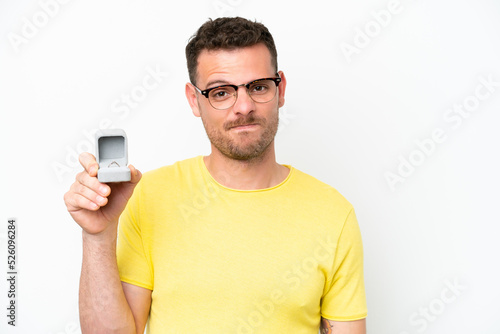 Young caucasian man holding a engagement ring isolated on white background with sad expression