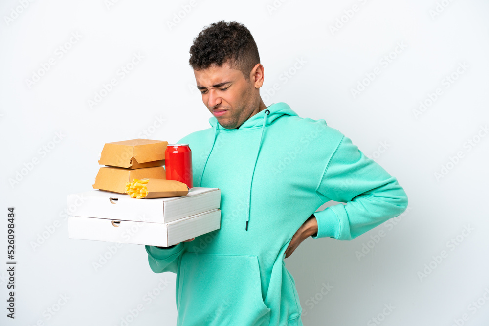 Young Brazilian holding fast food isolated on white background suffering from backache for having made an effort Young Brazilian holding fast food isolated on white background suffering from backache for having made an effort