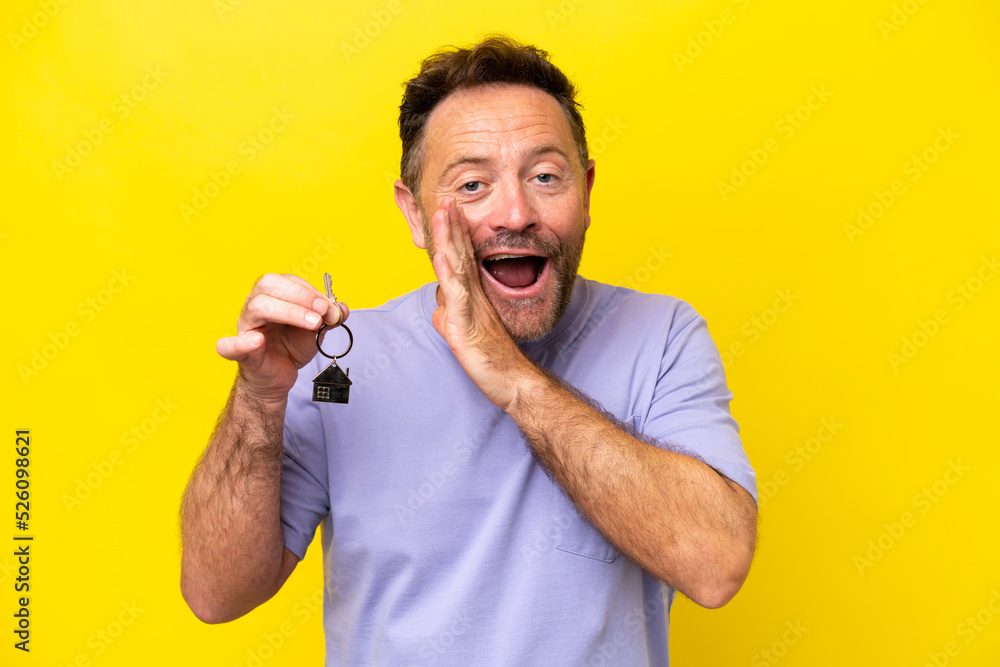 Middle age man holding home keys isolated on yellow background whispering something Middle age man holding home keys isolated on yellow background whispering something