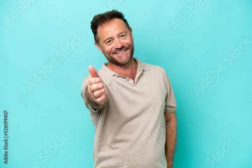 Middle age caucasian man isolated on blue background shaking hands for closing a good deal