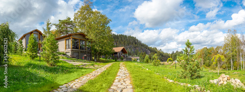 Modern village. Real estate in ecologically clean place. Panorama with rural town houses. Wooden cottages at foot hill. Summer landscape ECO village. Stone path leads to summer houses. ECO property photo