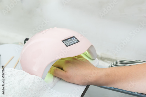 close-up of a latina girl's hand inside a 48 watt led nail lamp for semi permanent acrylic gel. woman getting a manicure for her personal nail care. pink lamp working properly.
 photo