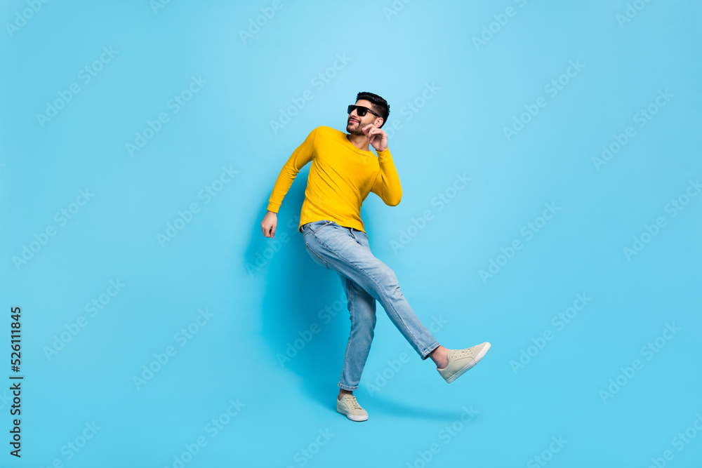 Full length photo of excited cool guy dressed yellow pullover dark eyewear dancing isolated blue color background Full length photo of excited cool guy dressed yellow pullover dark eyewear dancing isolated blue color background
