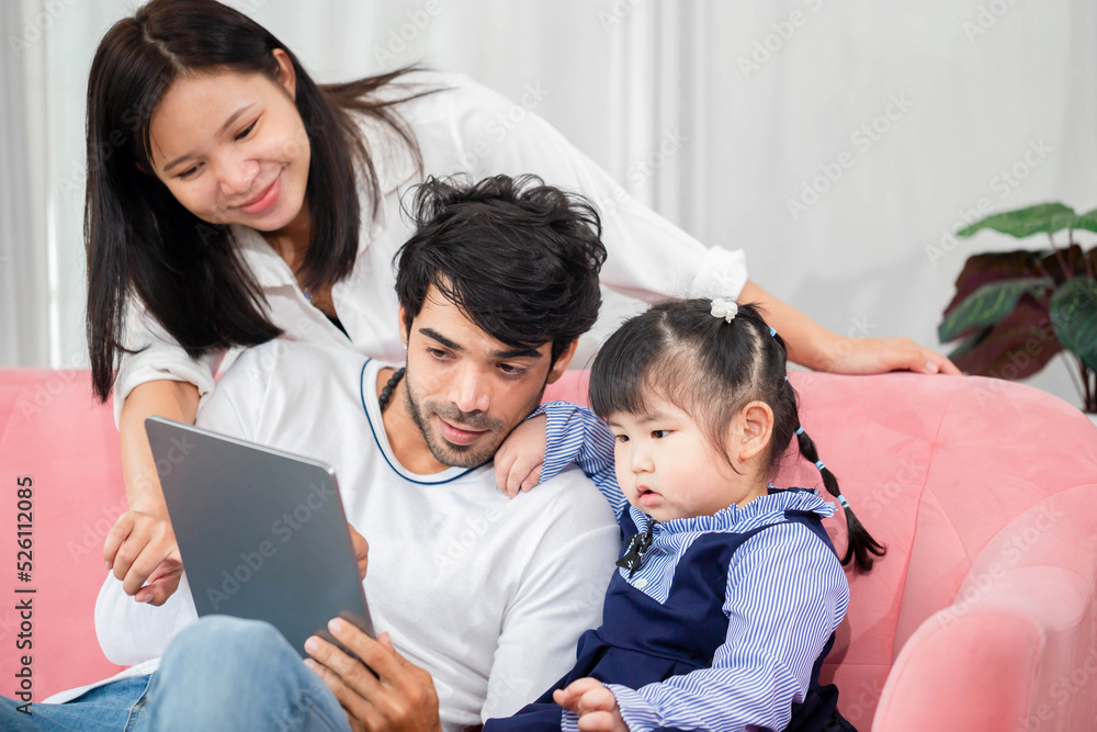 Family spending time on a sofa in the living room, Parents and daughter using digital tablet at home, Young family with child having fun using modern technology Family spending time on a sofa in the living room, Parents and daughter using digital tablet at home, Young family with child having fun using modern technology
