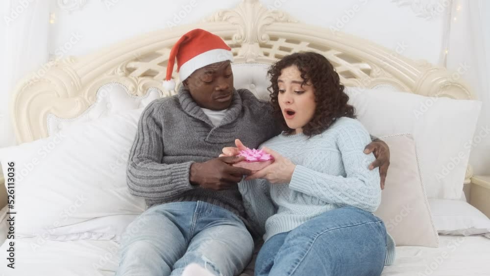 Man presenting christmas surprise gift to girlfriend in bed at home. Happy couple in love on a winter morning Man presenting christmas surprise gift to girlfriend in bed at home. Happy couple in love on a winter morning