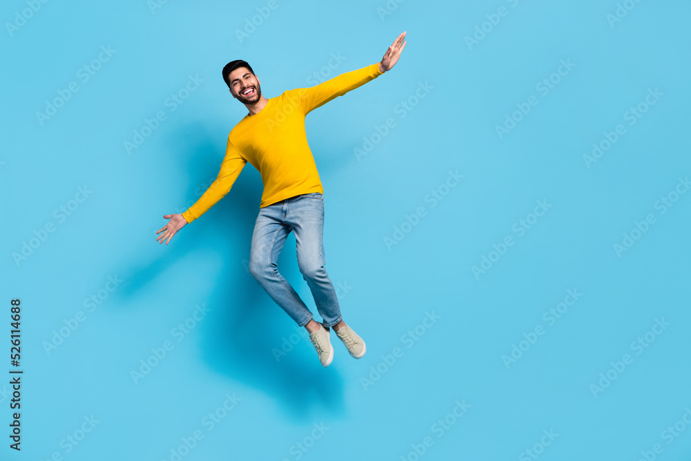 Full body portrait of active excited man hands wings jumping flight isolated on blue color background