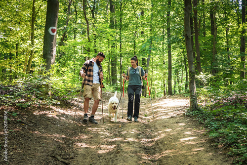 Young happy couple and their dog at hiking through the woods enjoying the sight. Two nature lovers in the mountain forest enjoy healthy walking through the nature. With film grain selective focus