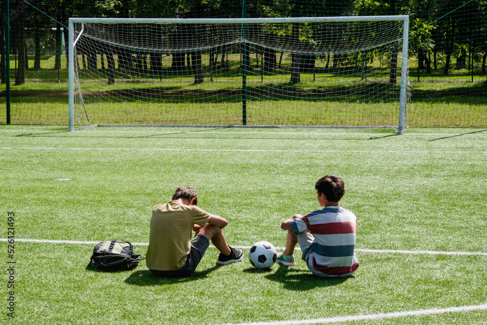 Fototapeta premium Teenagers talking in school stadium outdoors. Teenage boy comforting consoling upset sad friend. Education, bullying, conflict, problems at school, lost game, learning difficulties, empathy concept
