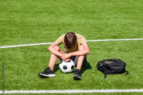 Fototapeta Naklejka Na Ścianę i Meble -  Sad alone teenage boy sitting in empty school sport stadium outdoors. Emotions, defeat, lost game, difficulties, problems of teenagers