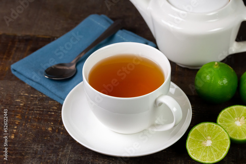 Hot tea in white cup with fresh lime on rustic wooden background.