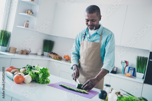 Photo of funny positive age man wear apron preparing supper cutting tasty vegetables indoors room home