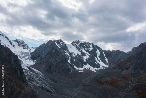 Atmospheric landscape with large snow mountain range with glacier and icefall in dramatic cloudy sky. Awesome high snowy mountains under rainy clouds. White snow on black rocks in overcast weather. © Daniil
