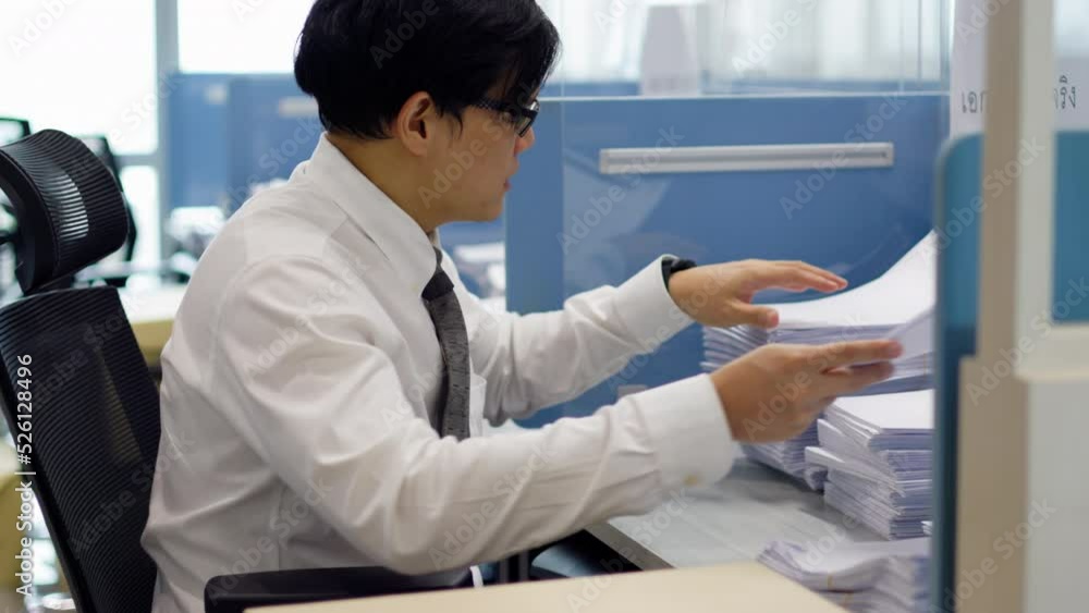 Overload office worker. Asian office worker is sitting at his desk clearing a lot of paperwork feel stressed and busy at the office. Overload office worker. Asian office worker is sitting at his desk clearing a lot of paperwork feel stressed and busy at the office.