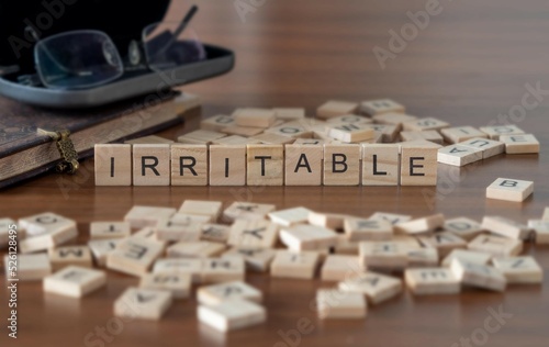 irritable word or concept represented by wooden letter tiles on a wooden table with glasses and a book