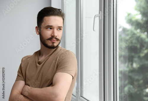 Handsome man near window indoors. Space for text