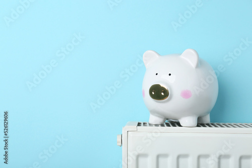 Piggy bank on heating radiator against light blue background, space for text