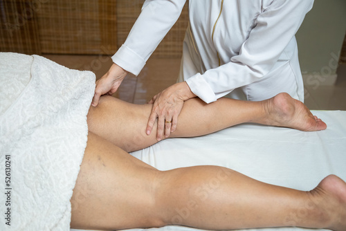 Um profissional fazendo massagem terapeutica nas pernas do paciente que está deitado em uma maca.