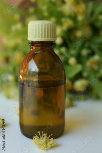 Bottle of essential oil and linden blossoms on white table, closeup