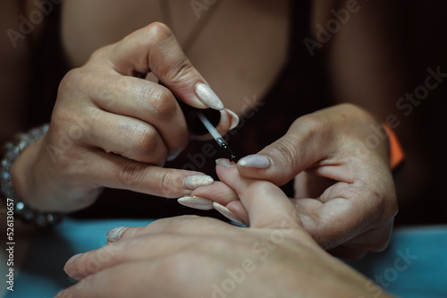 Manicurist hands paint nails on client's hand with varnish