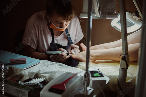 Masked pedicurist polish nails with electric pedicure machine photo