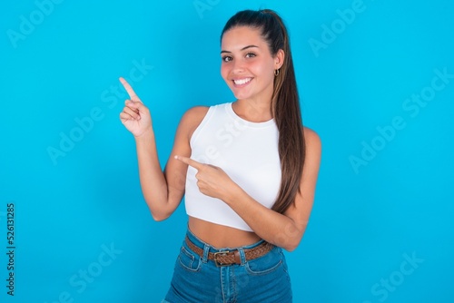 Canvas-taulu beautiful brunette woman wearing white tank top over blue background indicating