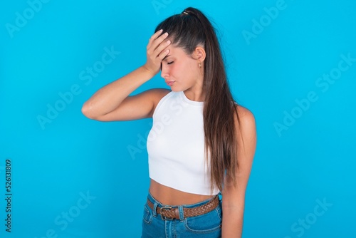 A very upset and lonely beautiful brunette woman wearing white tank top over blue background crying,