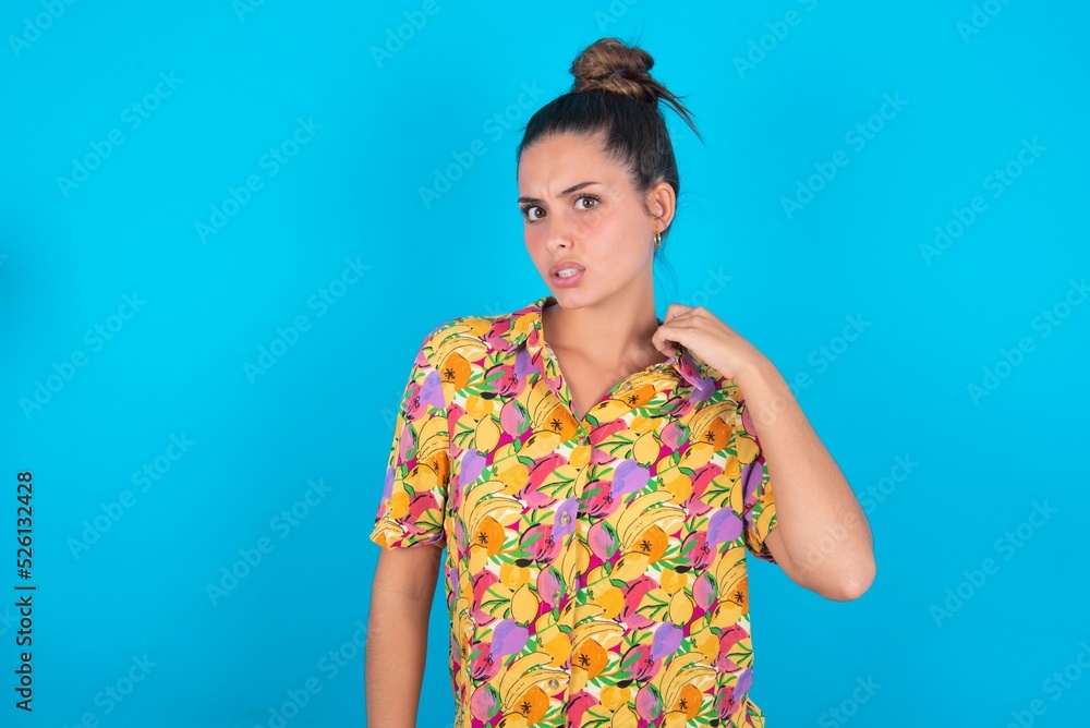 beautiful brunette woman wearing colourful shirt over blue background stressed, anxious, tired and frustrated, pulling shirt neck, looking frustrated with problem beautiful brunette woman wearing colourful shirt over blue background stressed, anxious, tired and frustrated, pulling shirt neck, looking frustrated with problem
