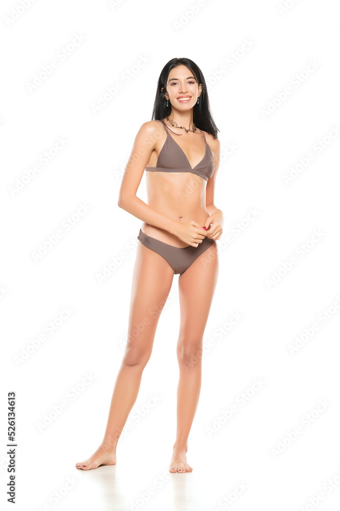 Young smiling brunette woman in bikini swimsuit posing on a white background. Young smiling brunette woman in bikini swimsuit posing on a white background.