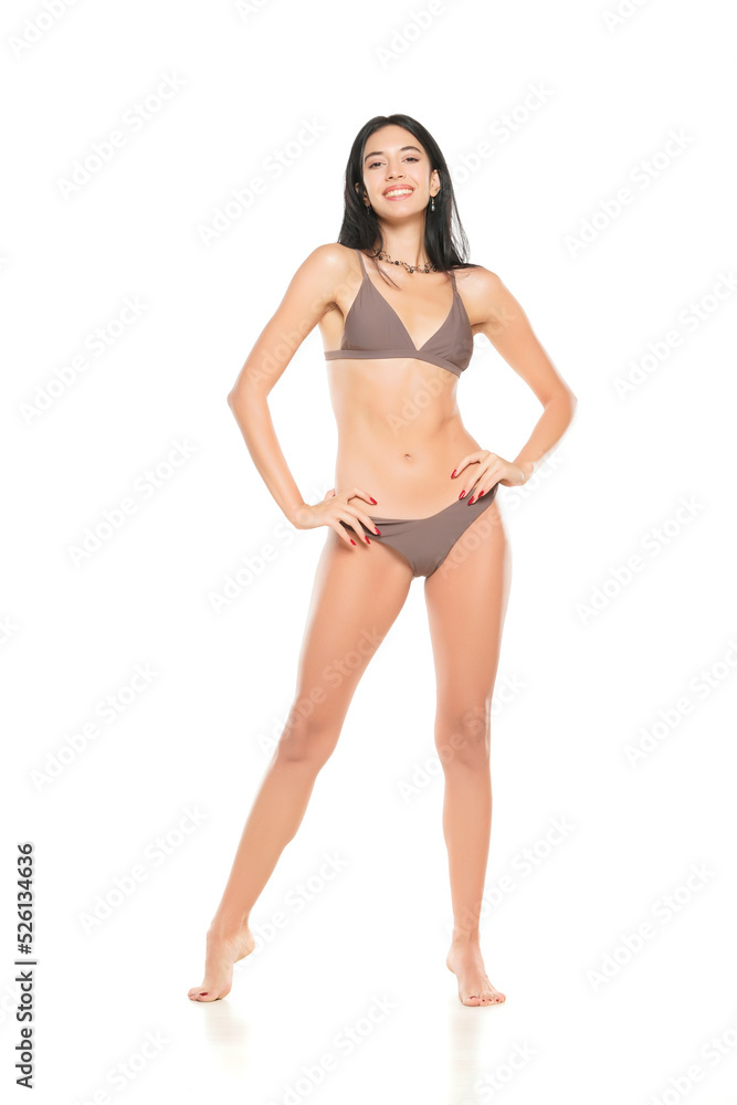 Young smiling brunette woman in bikini swimsuit posing on a white background. Young smiling brunette woman in bikini swimsuit posing on a white background.