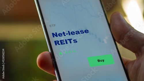 An investor's analyzing the real estate investment trusts reit on screen. A phone shows the ETF's prices net-lease REITs
