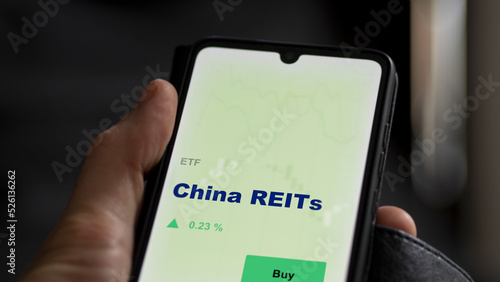 An investor's analyzing the real estate investment trusts reit on screen. A phone shows the ETF's prices China REITs