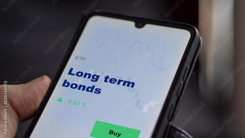 An investor's analyzing the stocks on screen. A phone shows the ETF's prices long term bonds An investor's analyzing the stocks on screen. A phone shows the ETF's prices long term bonds