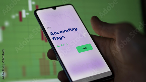 An investor's analyzing the accounting flags etf fund on screen. A phone shows the ETF's prices stocks to invest photo