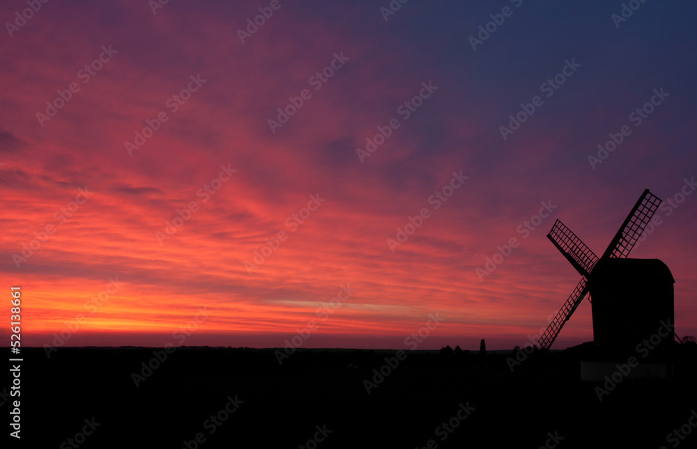 A windmill in Hertfordshire silhouetted by the pink-purple setting sun. 