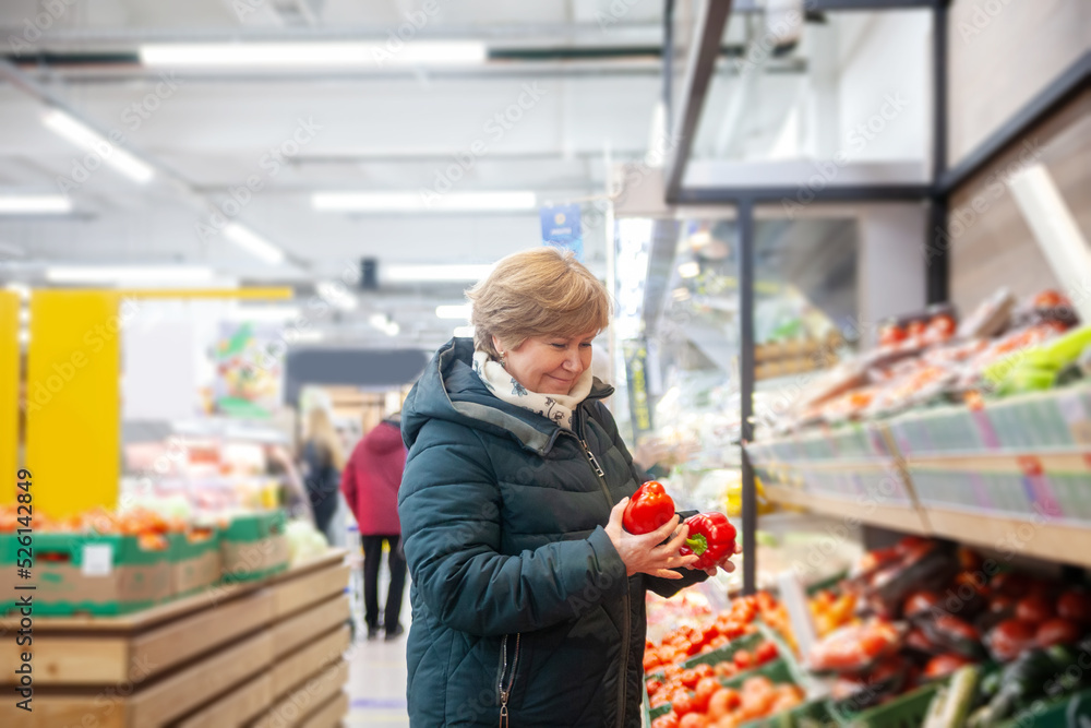 Smiling senior woman picking apple at the grocery shop