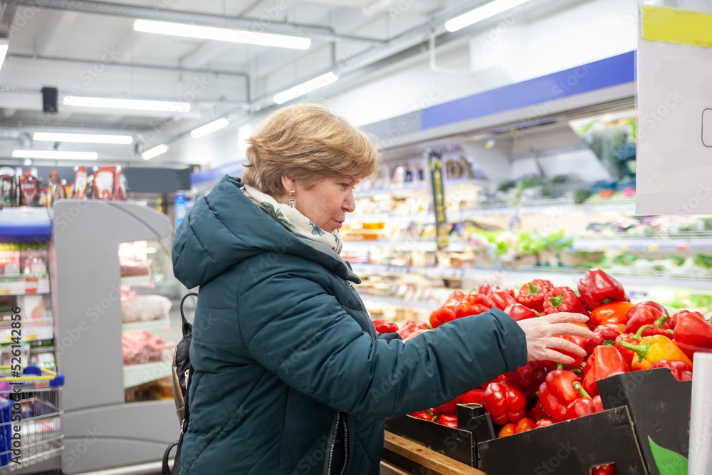 Smiling senior woman picking apple at the grocery shop