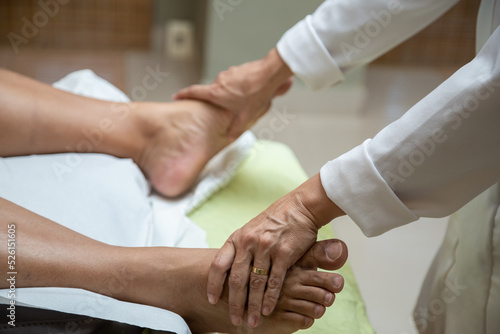 Um profissional fazendo massagem terapêutica nos pés do paciente que está deitado em uma maca.